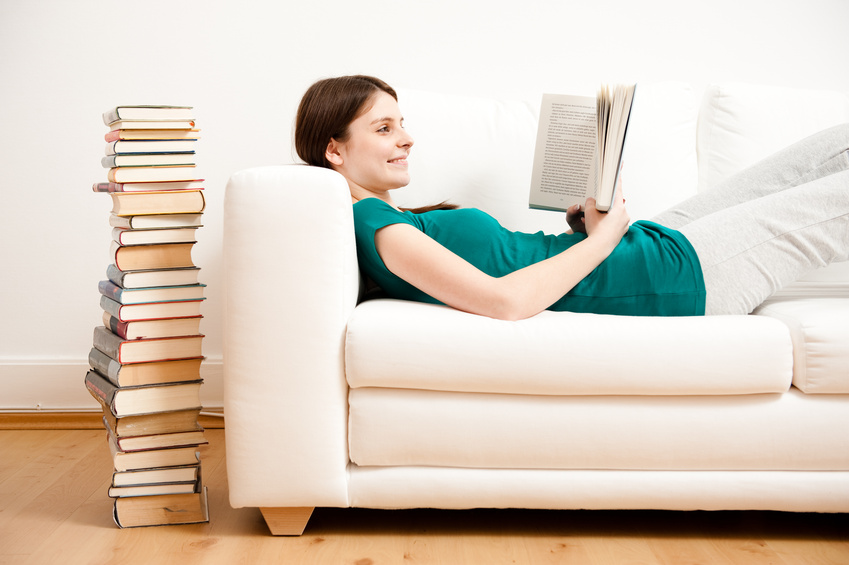 Junge Frau liest auf Sofa Buch